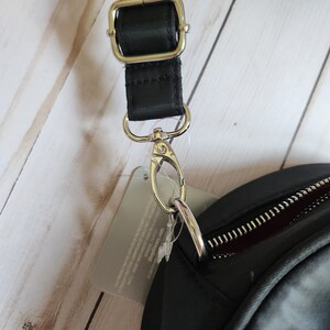 May include: A black crossbody bag with a silver zipper and a silver clasp. The bag has a black adjustable strap with a silver buckle.
