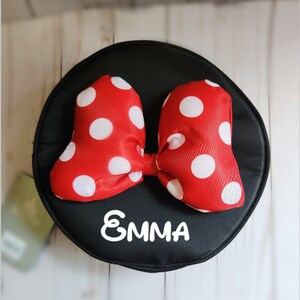 May include: A black round fabric pouch with a red and white polka dot bow and the name "EMMA" written in white.