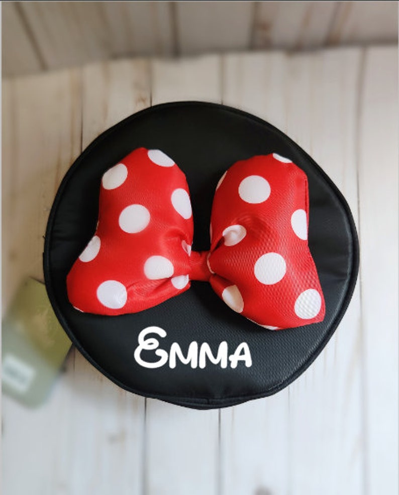 May include: A black round fabric pouch with a red and white polka dot bow and the name "EMMA" written in white.