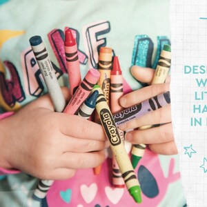 May include: A child's hands holding a collection of Crayola crayons in various colors, including blue, pink, and yellow. The image includes the text "DESIGNED WITH LITTLE HANDS IN MIND".