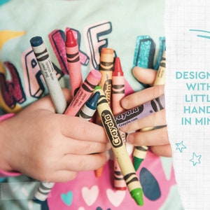 May include: A child's hands hold a collection of Crayola crayons in various colors, including blue, pink, and yellow. The image includes the text "DESIGNED WITH LITTLE HANDS IN MIND."