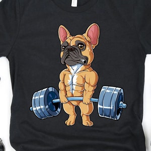 May include: Black t-shirt featuring a cartoon image of a French bulldog lifting weights. The bulldog is wearing a red collar and has a muscular physique.