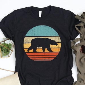 Puede incluir: Camiseta negra con un gr&aacute;fico retro de un oso caminando frente a una puesta de sol. El gr&aacute;fico tiene un aspecto vintage y desgastado con una combinaci&oacute;n de colores turquesa, naranja, amarillo y rojo.