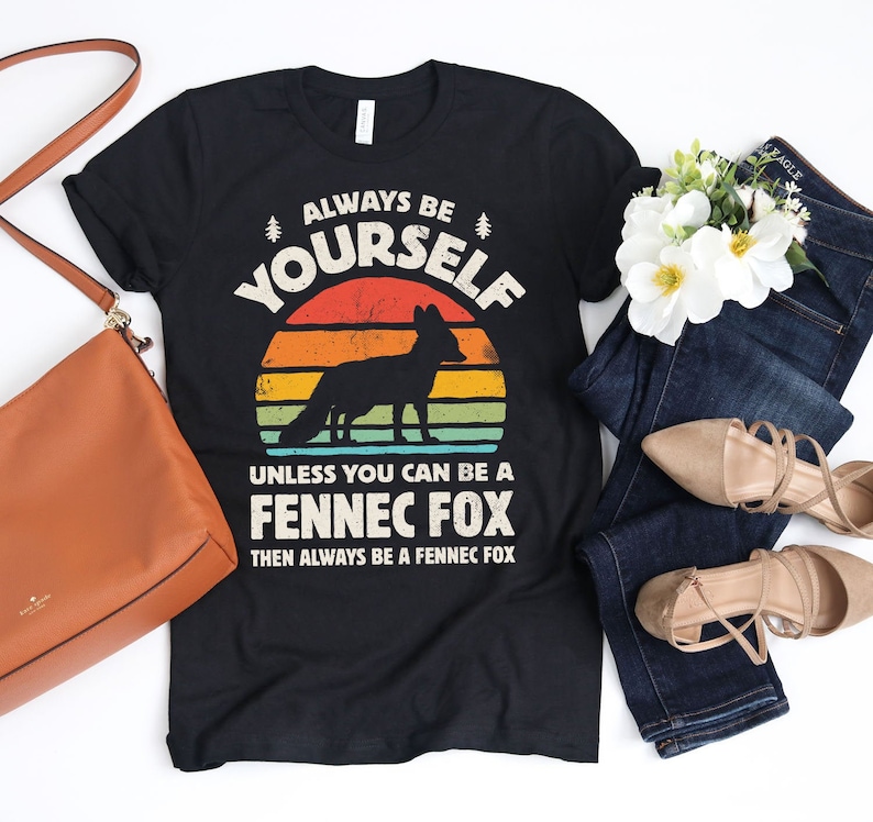 Peut inclure: T-shirt noir avec un graphique vintage d'un fennec devant un coucher de soleil. Le texte dit "Soyez toujours vous-m&ecirc;me &agrave; moins que vous ne puissiez &ecirc;tre un fennec, alors soyez toujours un fennec."