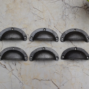 May include: Six black cast iron drawer pulls with a rounded, half-circle shape. The pulls are arranged in two rows of three.
