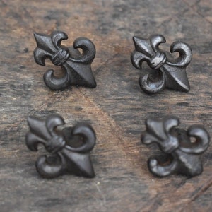 Puede incluir: Cuatro piezas de herrajes decorativos de metal negro en forma de flor de lis sobre una superficie de madera.