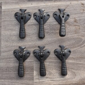 Könnte beinhalten: Sechs schwarze Schubladengriffe aus Gusseisen mit herzförmigem Design und einem Hebelgriff. Die Griffe sind in zwei Reihen zu je drei angeordnet.