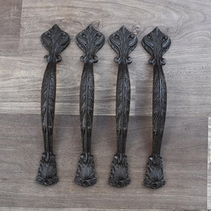 Puede incluir: Cinco tiradores de puerta de hierro fundido negro con diseños ornamentados. Los tiradores tienen un patrón de hojas y un remate puntiagudo.