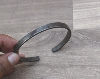 Puede incluir: Una pulsera de metal plateado con una superficie texturizada y una inscripción.