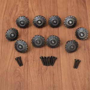 May include: Ten black metal cabinet knobs with a decorative floral design and matching screws.