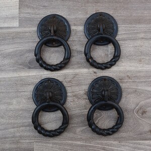 May include: Four black metal ring door handles with a decorative floral design. Each handle has a twisted rope-like ring.