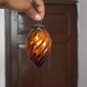 Könnte beinhalten: Ein brauner Weihnachtsbaumschmuck aus Glas mit einem Spiralmuster. Der Schmuck hat eine silberne Kappe und eine Schlaufe zum Aufhängen.