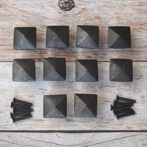 May include: A collection of ten dark gray, square cabinet knobs with a pyramid design, arranged on a light brown wooden surface. Also included are three sets of black screws, perfect for furniture or home decor projects.