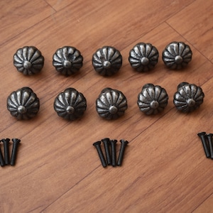 May include: Twelve silver-toned metal cabinet knobs with a decorative flower design and twelve black screws.