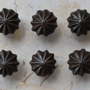 May include: Six black cast iron drawer pulls with a starburst design. Each pull has a raised center and a slightly textured surface.