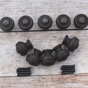 Puede incluir: Un juego de diez pomos redondos para armarios en color negro mate con un perfil escalonado. Los pomos presentan una cúpula circular central y una base cónica. Se incluyen dos pequeños montones de tornillos de montaje de metal negro a juego.