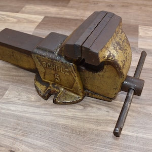 Könnte beinhalten: Ein alter gelber und brauner Schraubstock aus Metall mit einem schwarzen Griff. Der Schraubstock trägt die Aufschrift "SCHULZ" und die Nummer "5" an der Seite.