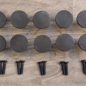 Op de afbeelding: Twaalf ronde zwarte kastknoppen met een rustieke afwerking en twaalf zwarte schroeven.