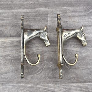Puede incluir: Dos perchas de pared de metal vintage, cada una con un diseño de cabeza de caballo. Los ganchos son de color plateado con ganchos de latón. Las cabezas de caballo están detalladas. Un artículo decorativo para el hogar.