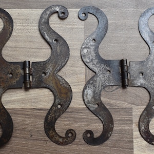 Peut inclure: Deux charnières anciennes en fer ornées d'un motif en S décoratif. Les charnières sont rouillées et ont une patine brun foncé.