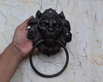 Puede incluir: Un llamador de puerta de hierro fundido negro en forma de cabeza de león con un anillo circular para tirar.