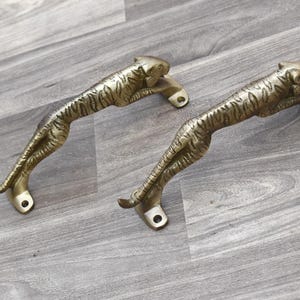 以下が含まれることがあります： 虎の形をした金色の金属製のドアノブが2つ。ノブは虎の縞模様で詳細に作られており、磨かれた仕上げになっています。