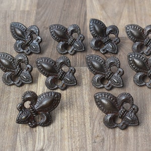 May include: Twelve ornate, dark brown metal fleur-de-lis drawer pulls with a detailed design.