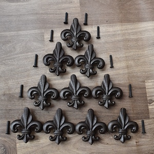 Pode incluir: Nove peças de ferragens decorativas de metal preto em forma de flor-de-lis com parafusos.