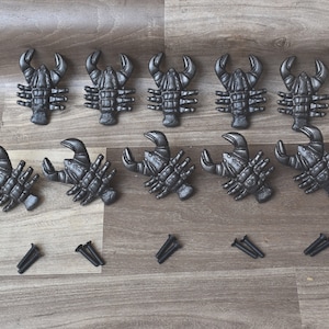 以下が含まれることがあります： ネジ付きの黒い金属製のロブスターの引き出しノブが10個。ロブスターのノブは2列に5個ずつ並んでいます。