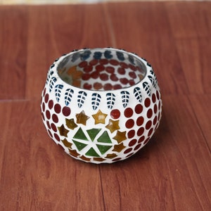 Op de afbeelding: Een ronde glazen kaarsenhouder met een mozaïekontwerp. De mozaïek heeft rode, witte, groene en gouden tegels in een geometrisch patroon.