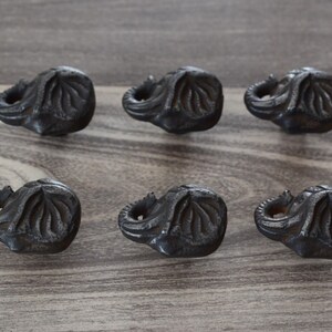 May include: Six black metal elephant-shaped drawer pulls. The pulls are detailed with textured lines and have a slightly distressed finish.