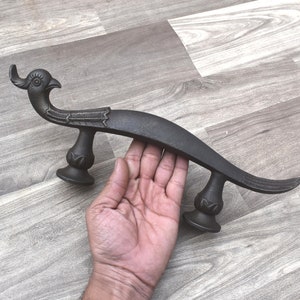 Könnte beinhalten: Ein schwarzer Türknauf aus Metall in Form eines stilisierten Vogels mit einem geschwungenen Körper und einem detaillierten Kopf. Der Knauf hat zwei dekorative Sockel.