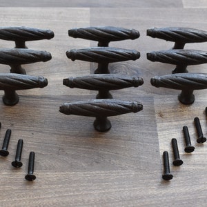 May include: Ten black metal drawer pulls with a twisted rope design and a T-shaped handle. The pulls are arranged in three rows with screws below.