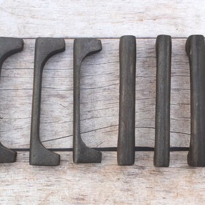May include: Six dark charcoal-colored metal drawer pulls arranged in two rows of three. The three pulls on the left feature a curved, arched design, while the three pulls on the right are straight, cylindrical bars with a matte, textured finish.