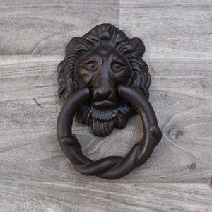 Puede incluir: Un llamador de puerta de hierro fundido negro en forma de cabeza de león con un anillo de cuerda trenzada.