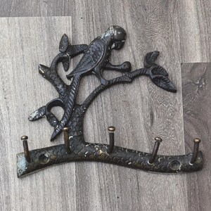May include: A metal key holder shaped like a tree with a parrot perched on a branch. The tree has five hooks for hanging keys.