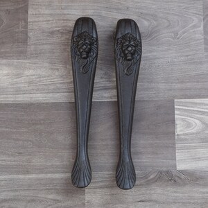 May include: Two black metal door handles with lion head designs.