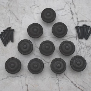 Può includere: Dieci pomelli per armadi in metallo nero con un design floreale decorativo, disposti a forma di triangolo su una superficie di marmo bianco. I pomelli sono forniti con viti per l'installazione.