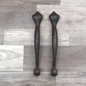 May include: Two black metal door handles with a pointed top and a rounded bottom.