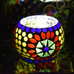 May include: A round glass candle holder with a mosaic design. The mosaic features blue, red, yellow, and green glass pieces.