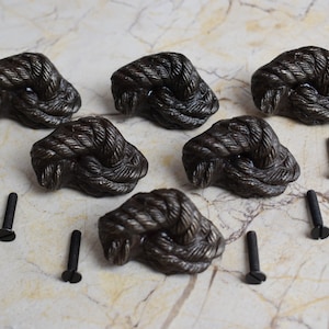 May include: Six dark brown rope knot drawer pulls with black screws. The pulls are made to look like a knotted rope.