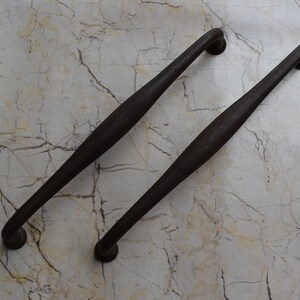 May include: Two black metal door handles with a rounded end. The handles are on a white marble background.