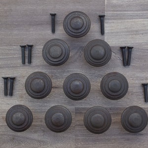 Peut inclure: Douze boutons de porte en métal noir avec un motif de cercles concentriques et des vis assorties.
