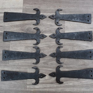 May include: Eight black metal hinges with a fleur-de-lis design. The hinges are arranged in four rows of two, with the fleur-de-lis facing outwards.