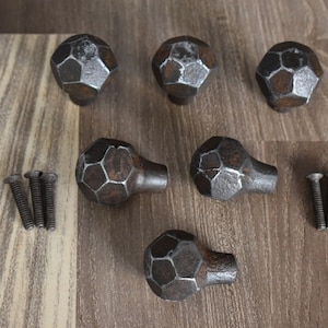 May include: Six rustic, dark gray metal cabinet knobs with a geometric design. The knobs have a slightly hammered finish and come with six matching screws.