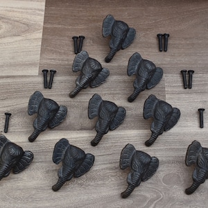 May include: Ten black cast iron elephant head drawer pulls with screws. The pulls have a detailed elephant head design with a trunk that curves upward.