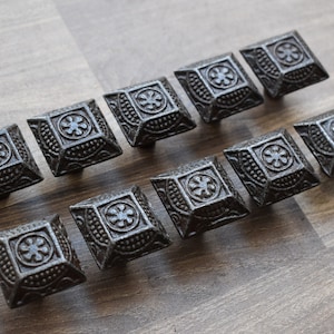 Puede incluir: Diez pomos de armario de hierro fundido negro con forma cuadrada y un diseño floral decorativo.