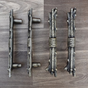 Puede incluir: Cinco pomos de armario rústicos con un acabado de madera. Los pomos tienen forma de ramas con un nudo atado alrededor del centro. Los pomos están dispuestos en una fila sobre una superficie de madera.