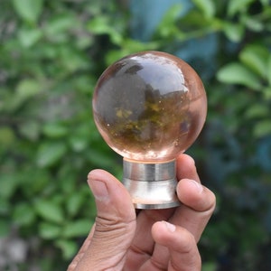 May include: A clear glass sphere with a silver base. The sphere is slightly pink and has a cloudy appearance.