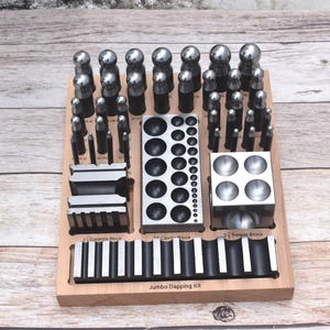Peut inclure: Un kit de formage métallique avec une base en bois contenant divers outils en acier. L'ensemble comprend de nombreux poinçons sphériques, un bloc à emboutir rectangulaire, un bloc à gorge et un long bloc rainuré marqué Jumbo Dapping Kit.